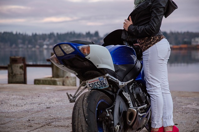 Žena v bielych nohaviciach stojí pri motorke.jpg