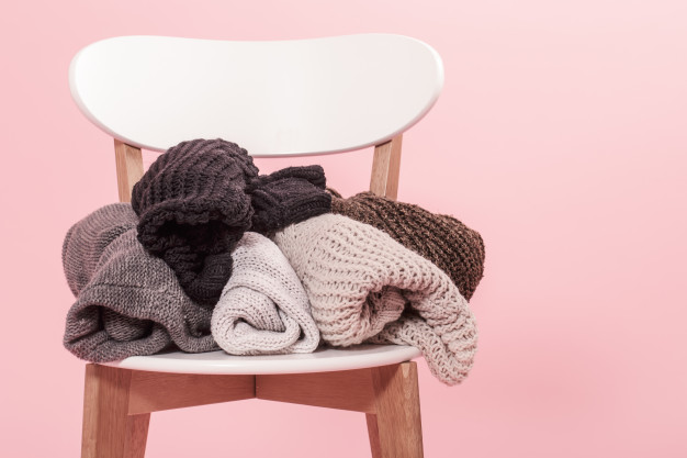 white-chair-with-stack-knitted-sweaters-pink-background_169016-3383